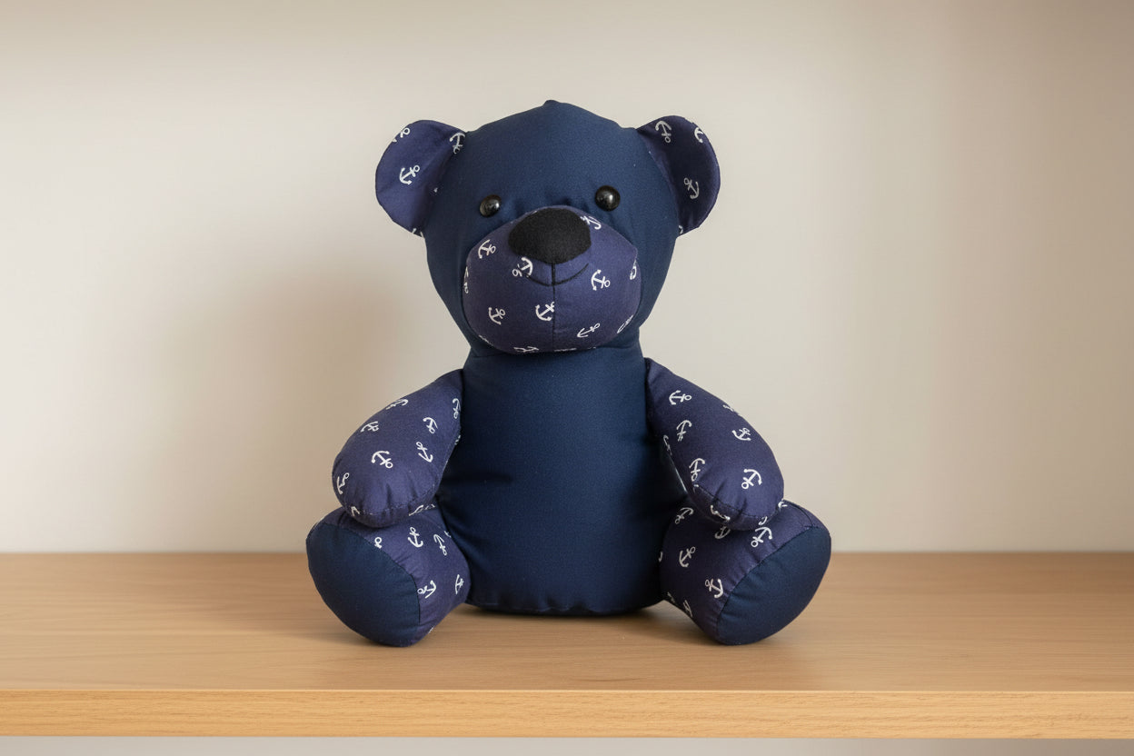 Navy blue teddy bear with anchor pattern on a wooden shelf against a beige wall