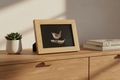 Wooden picture frame with a bird illustration on a wooden surface with a plant and books.