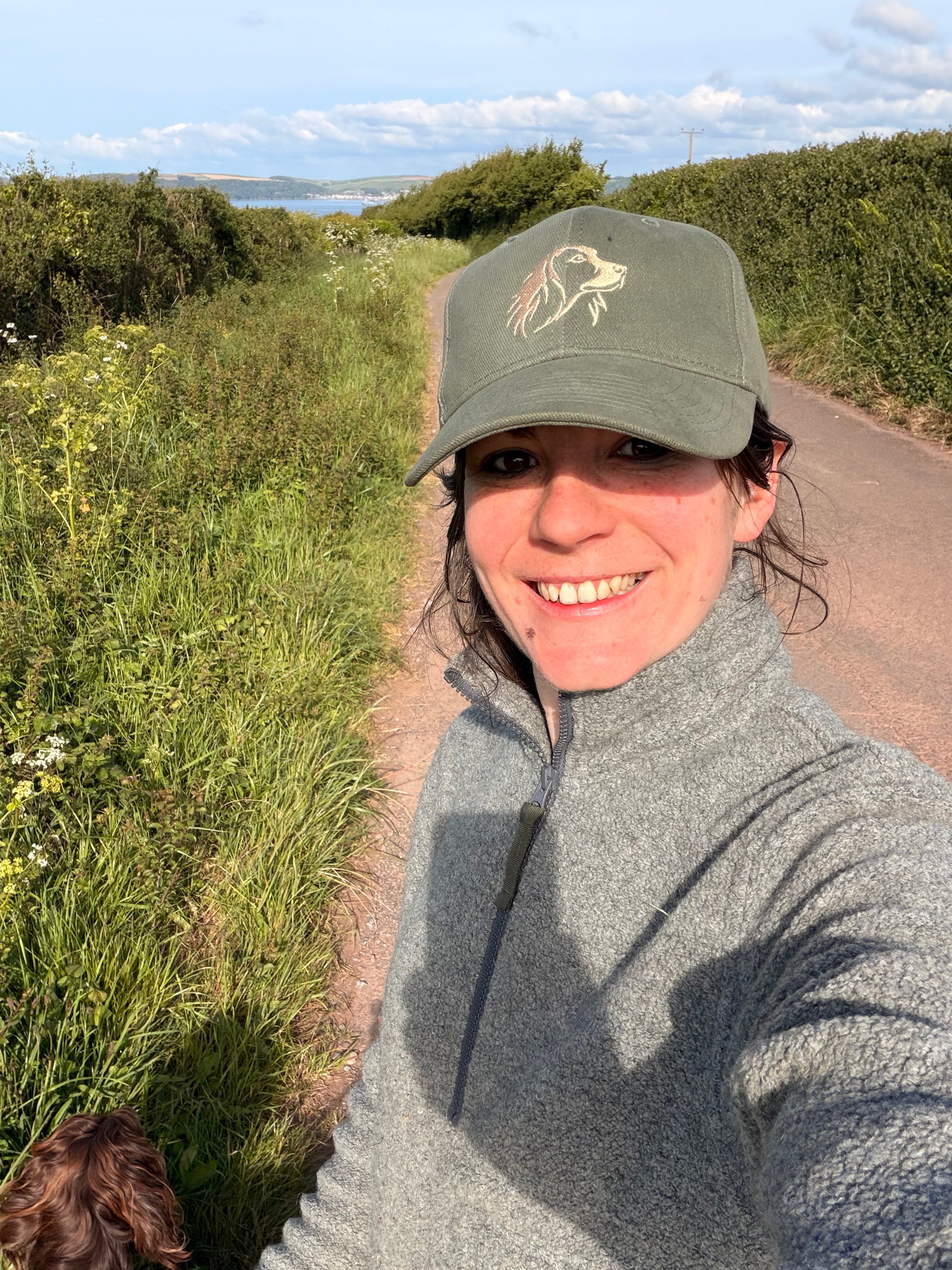Person wearing green cap with a subtle embroidered spaniel on the front, while out on a walk 