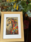 Framed artwork of a colorful horse portrait with a wooden frame, surrounded by greenery.