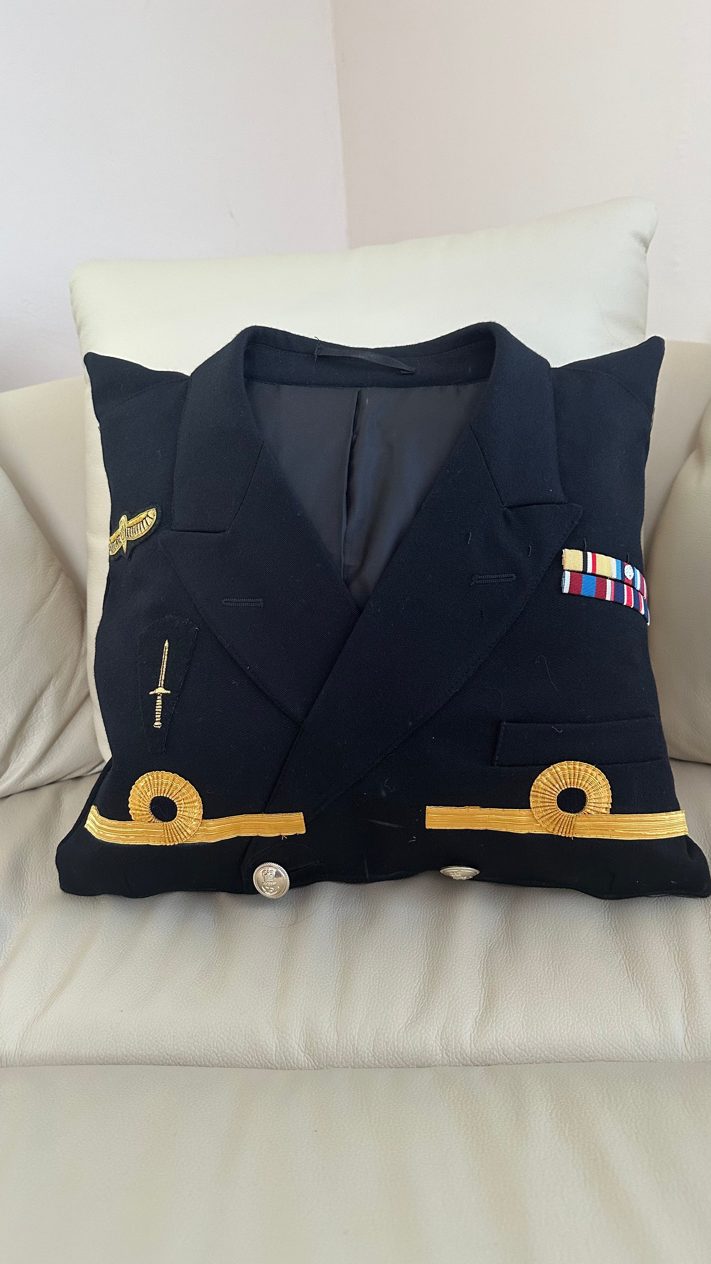 Navy blue military uniform jacket pillow with gold accents on a white couch.