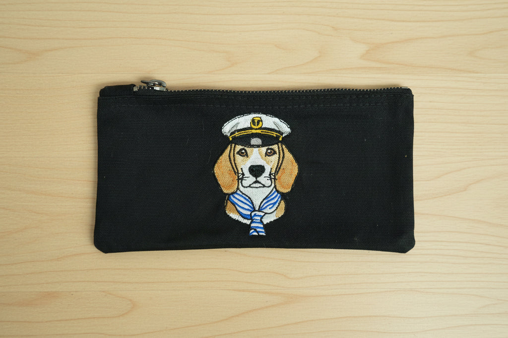 Black pouch with a dog illustration wearing a captain's hat on a wooden surface