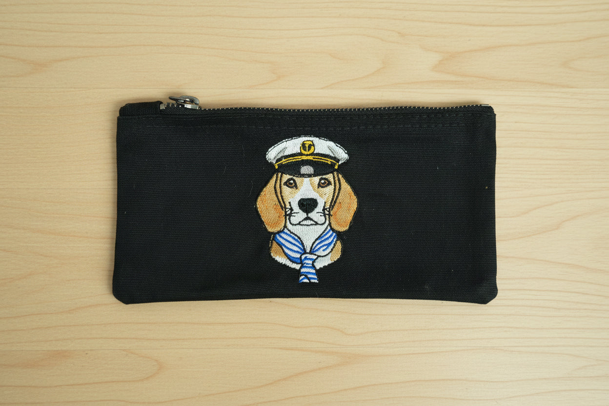 Black pouch with a dog illustration wearing a captain's hat on a wooden surface