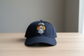 Navy blue cap with a dog illustration in a sailor hat on a wooden surface.