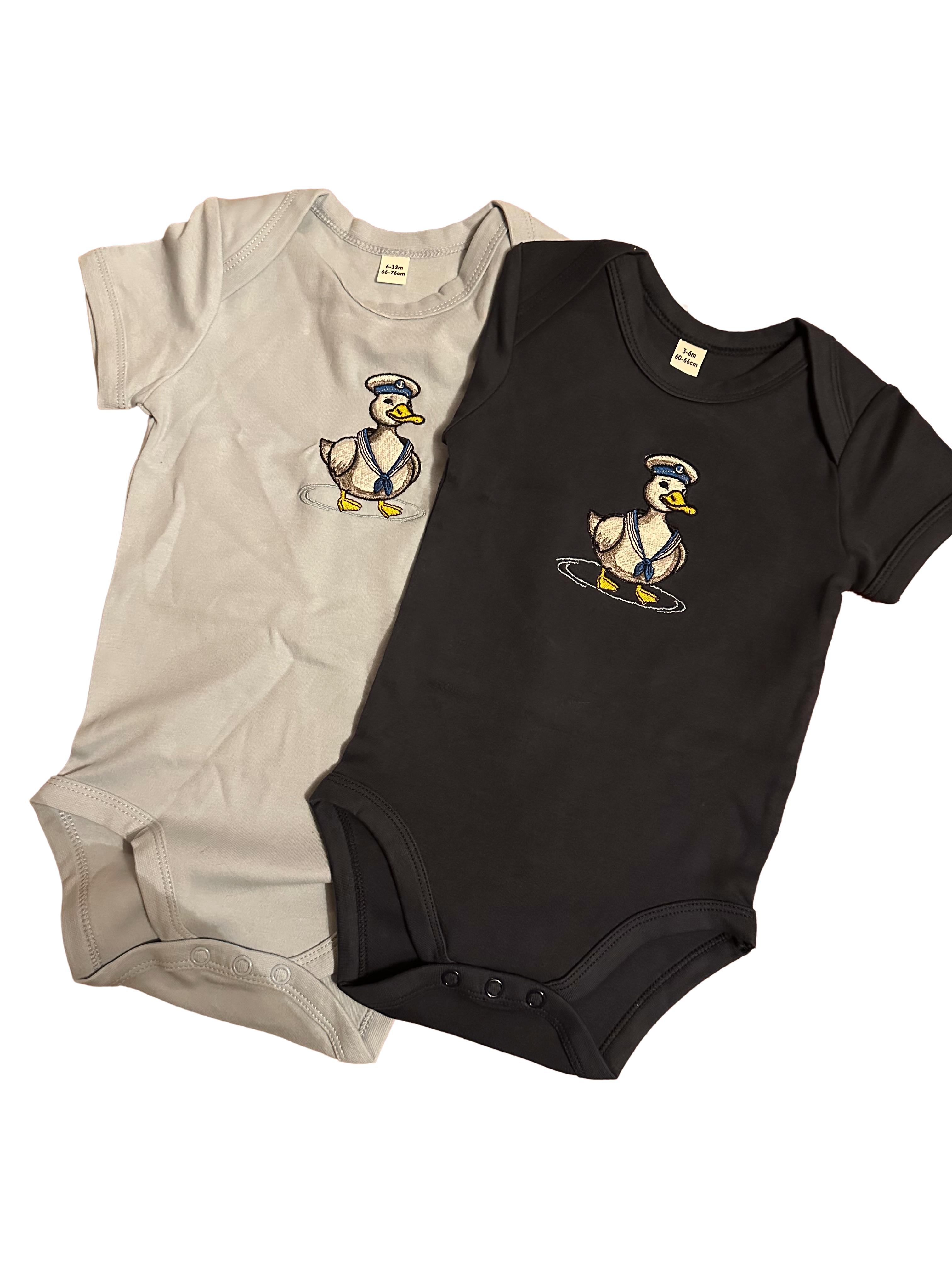 Two baby bodysuits, one light blue and one navy, with sailor duck designs. 