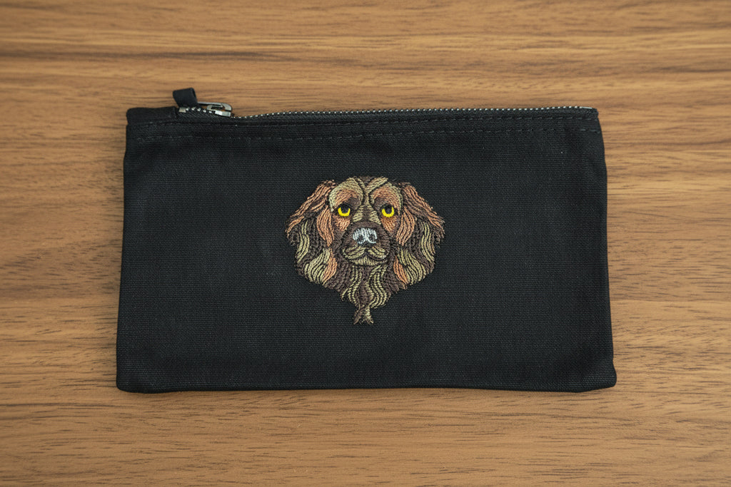 Black pouch with embroidered dog design on a wooden surface