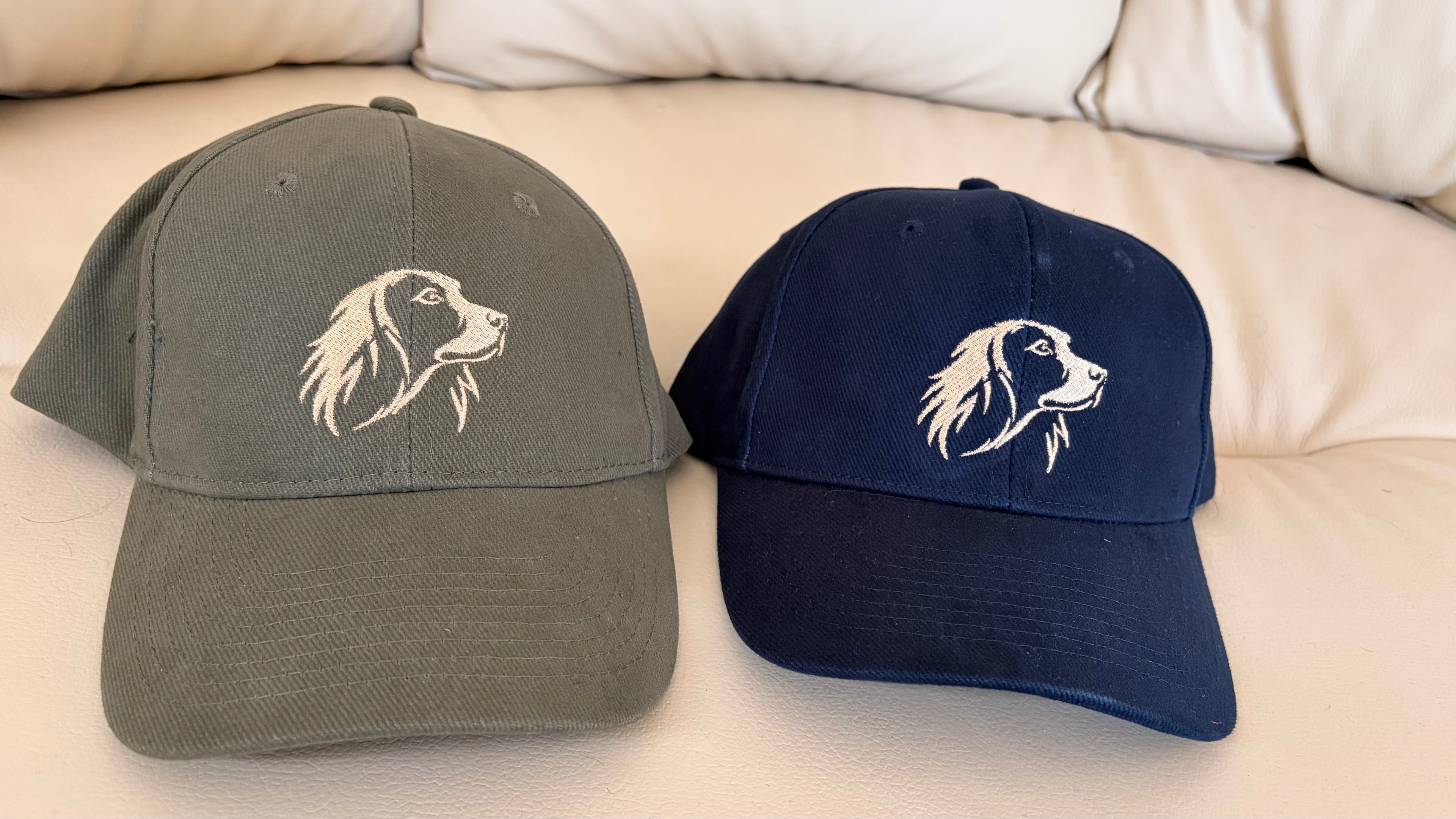 Two baseball caps with embroidered dog designs on a beige surface.