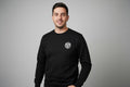 Man wearing a black sweatshirt with an anchor logo on a grey background
