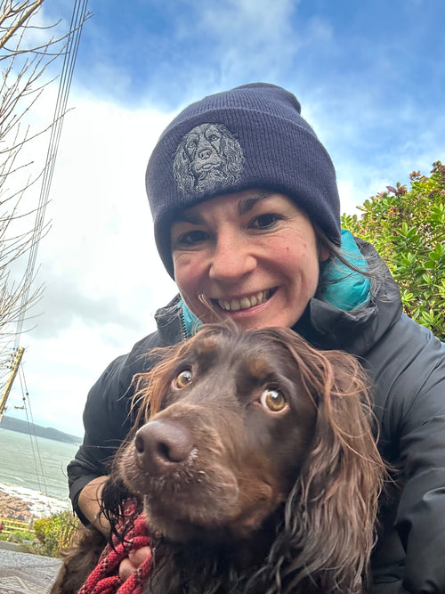 Person wearing a beanie with a dog outdoors near water
