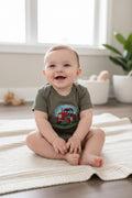 Baby sitting on a rug wearing a onesie with a red tractor graphic
